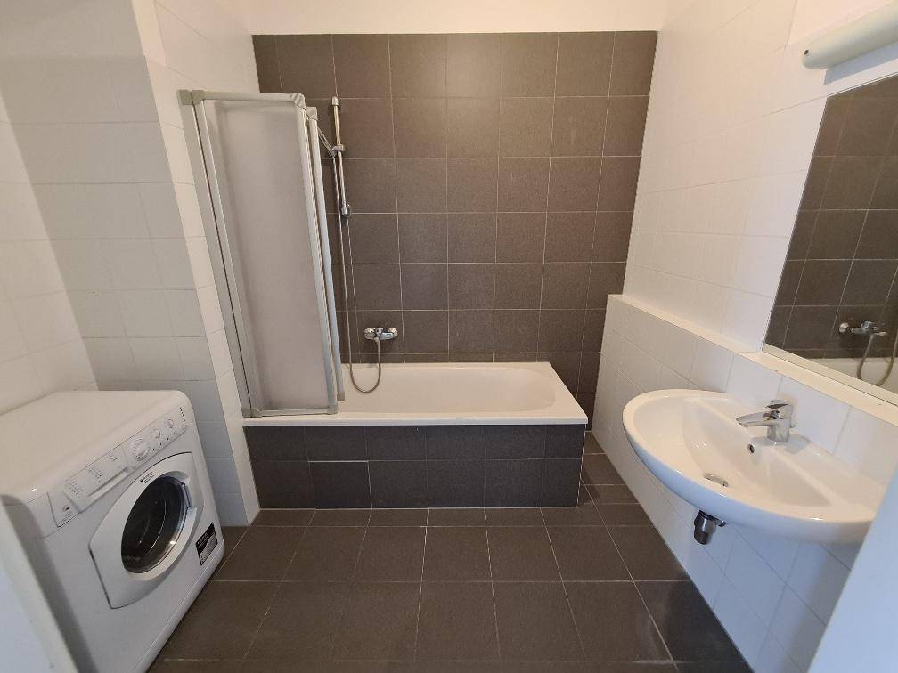 Modernes Badezimmer mit Badewanne, Dusche, Waschbecken und Fliesen in Grau und Weiß.