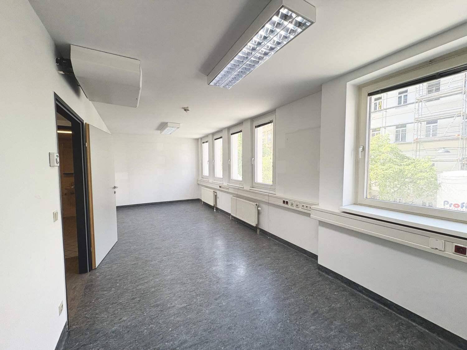 Langer Bürogang mit grauen Böden, vielen Fenstern und effizienter Deckenbeleuchtung.