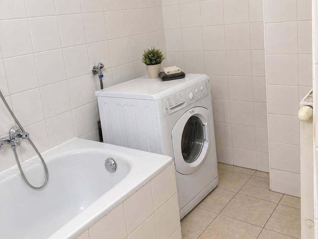 Badezimmer mit weißen Fliesen, Badewanne und einer Waschmaschine, funktional eingerichtet.