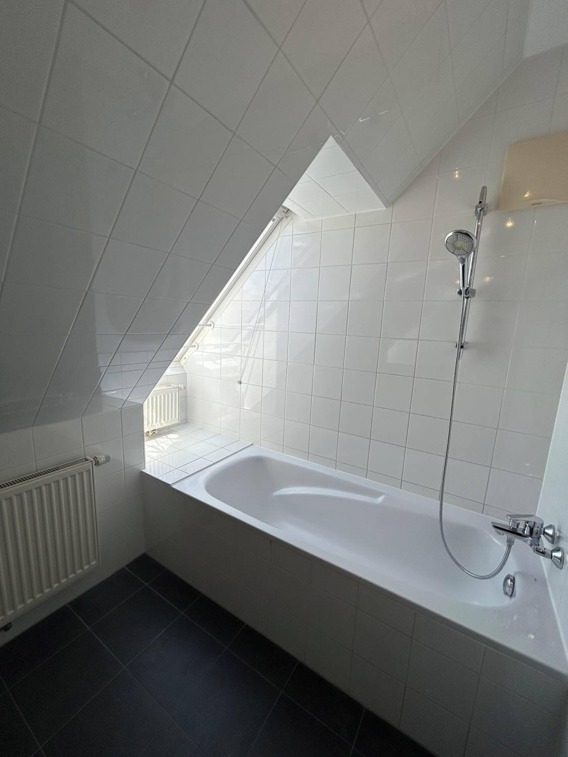 Modernes Badezimmer mit Badewanne, weißen Fliesen und Dachfenster.