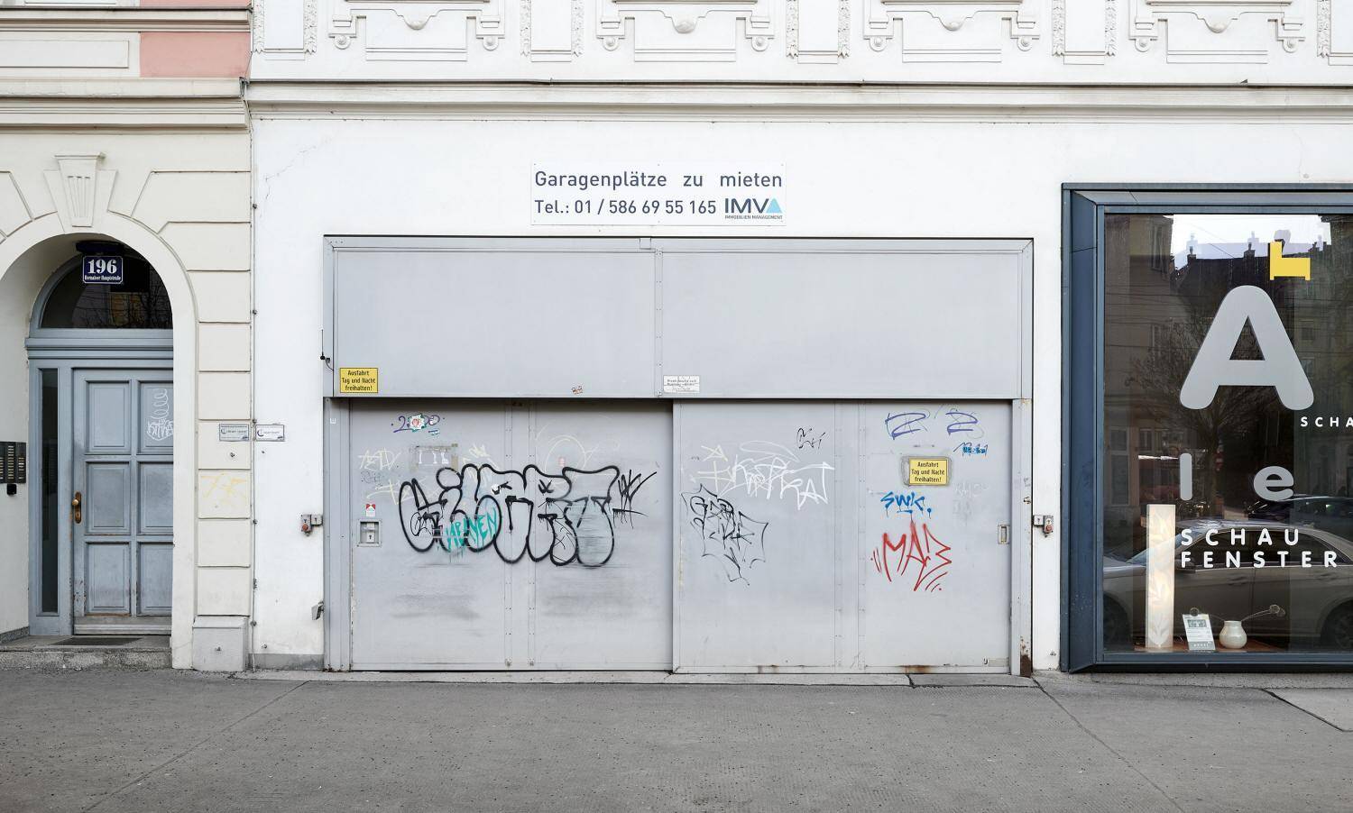 Garagentor im Erdgeschoss mit Graffiti und Hinweisschild für Mietparkplätze.