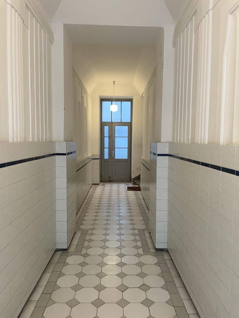 Eingangsbereich mit gefliesten Wänden und Boden, der zu einer Holztür führt.