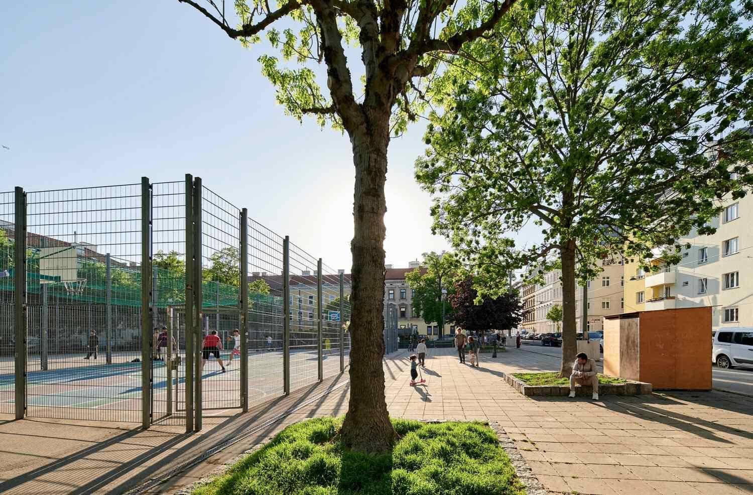 Öffentlicher Sportplatz mit Zaun, Bäumen und Menschen, der die Freizeitmöglichkeiten in der Umgebung zeigt.