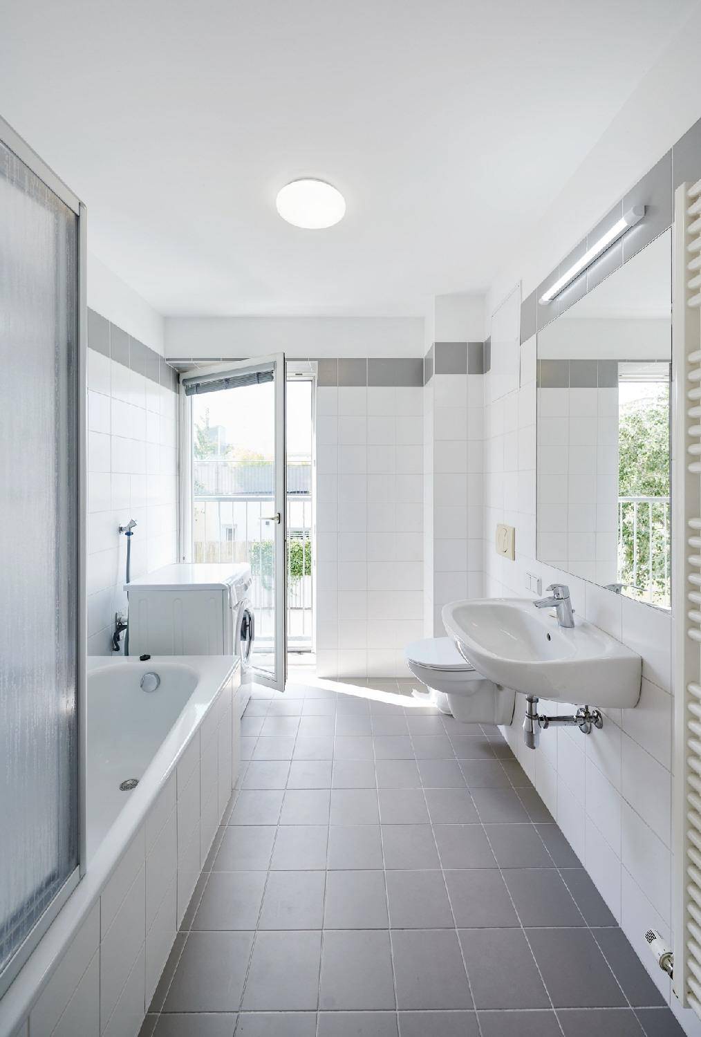 Modernes Badezimmer mit Badewanne, Waschbecken, WC und Waschmaschine, mit Balkonzugang.