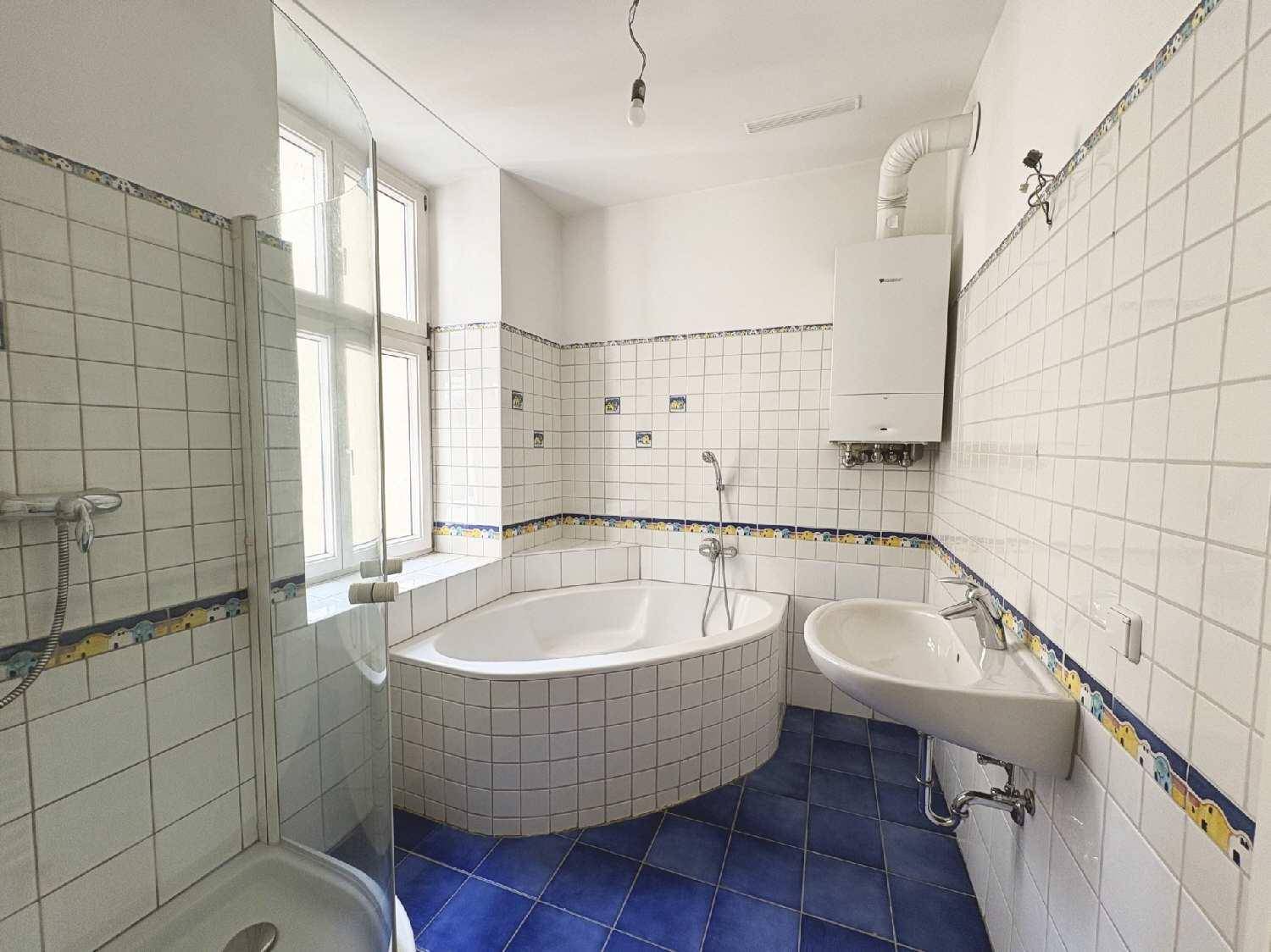 Badezimmer mit Eckbadewanne, Dusche, Waschbecken und Fenster, ausgestattet mit blauen Fliesen.