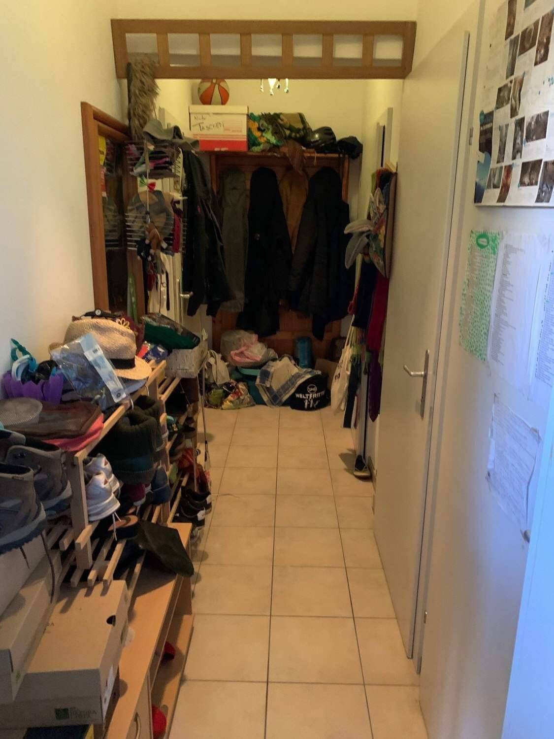 Schmaler Flur mit Fliesenboden, Schuhregalen und Garderobe für Kleidung und Accessoires.