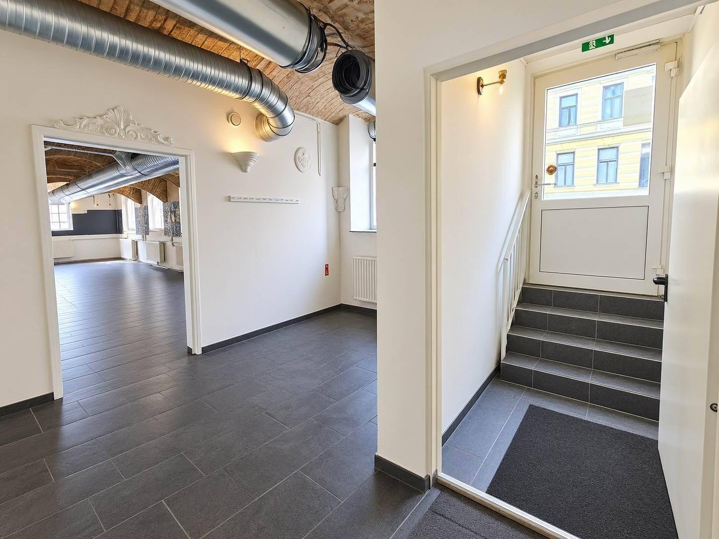 Eingangsbereich mit Treppe, Fliesenboden und Blick in den großen Gewerberaum.