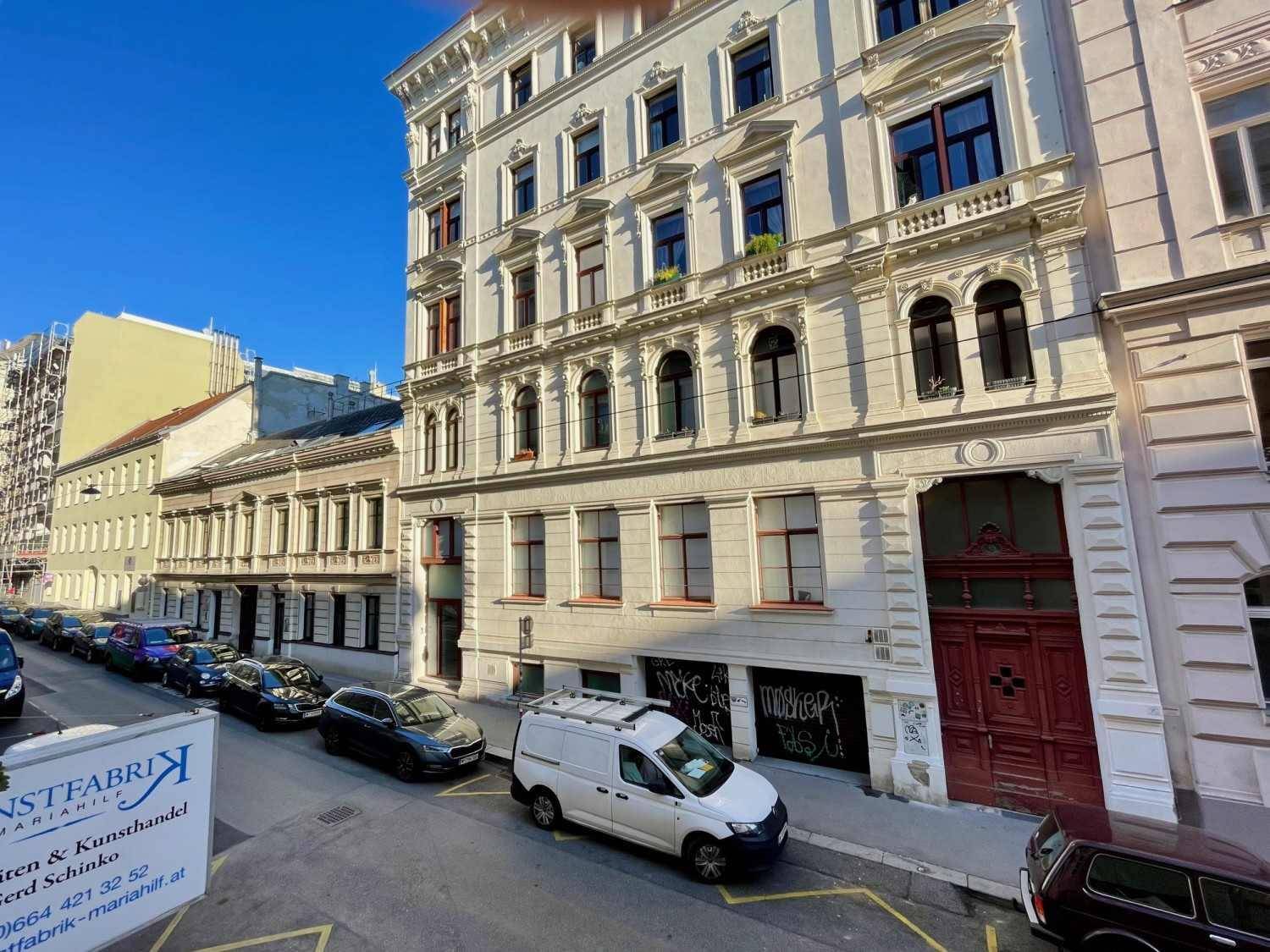 Ornates Gebäude mit Stuckfassade und großen Fenstern an einer sonnigen Stadtstraße.