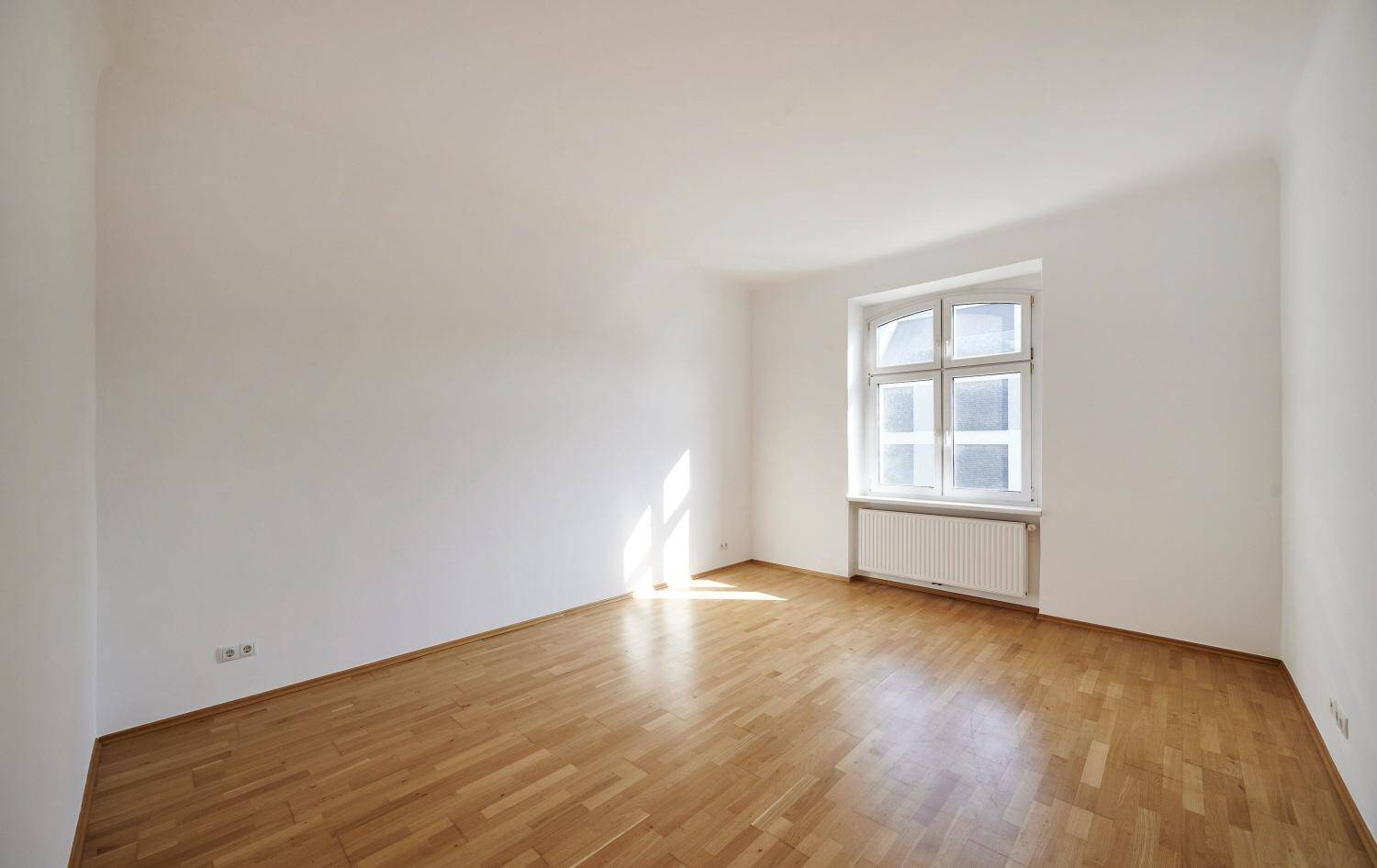 Geräumiges, helles Zimmer mit Holzboden und einem großen Fenster, ideal für individuelle Gestaltung.