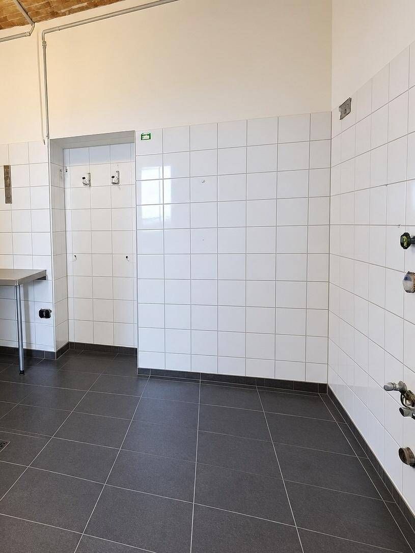 Gefliester Raum mit Hakenleiste und Anschlussmöglichkeiten, ideal als Vorbereitungs- oder Spülbereich.