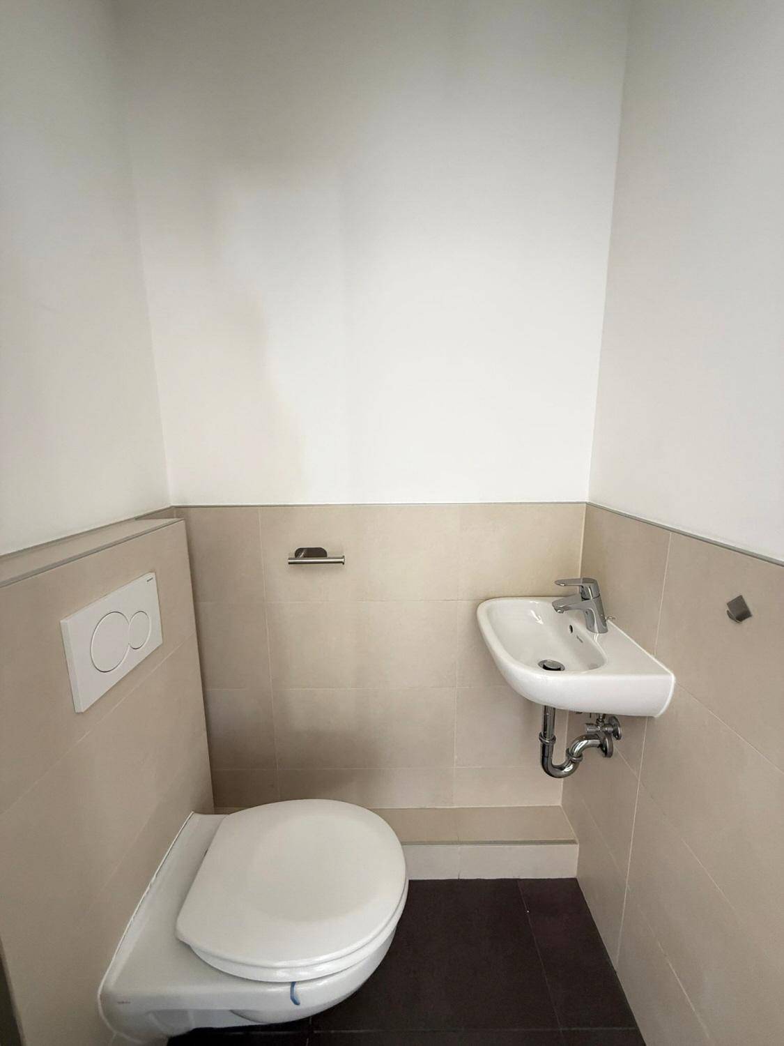 Modernes Gäste-WC mit Wand-WC und kleinem Waschbecken, in hellen Fliesen gehalten.