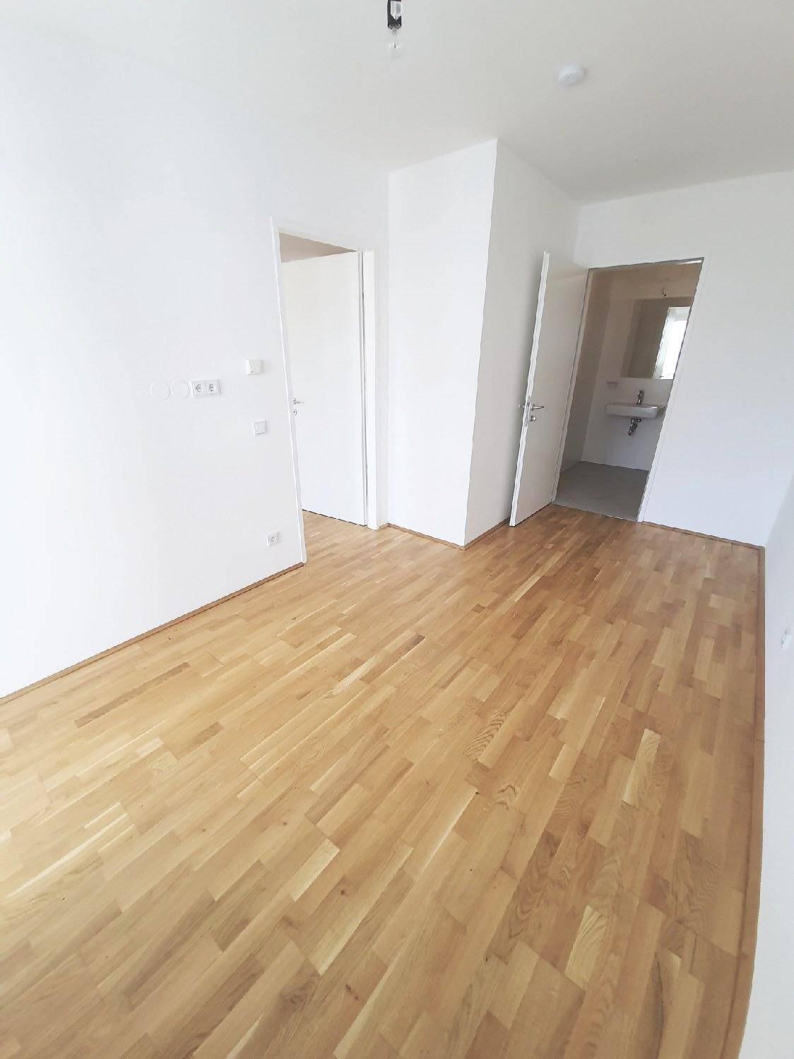 Heller Raum mit Parkettboden und weißen Wänden, der Zugänge zu angrenzenden Zimmern bietet.