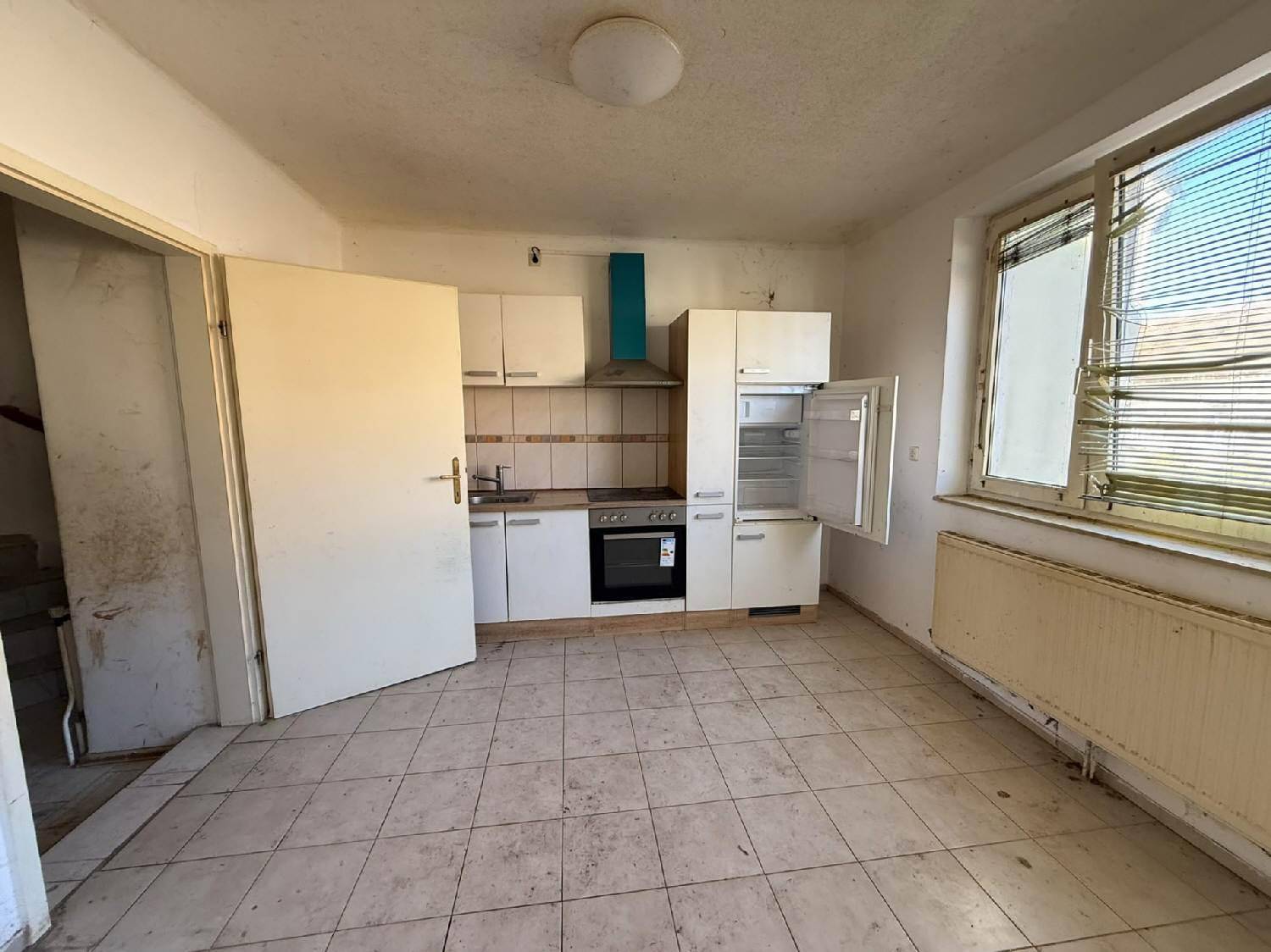 Küche mit Einbauschränken, Herd und Kühlschrank, gefliest und mit Fenster.