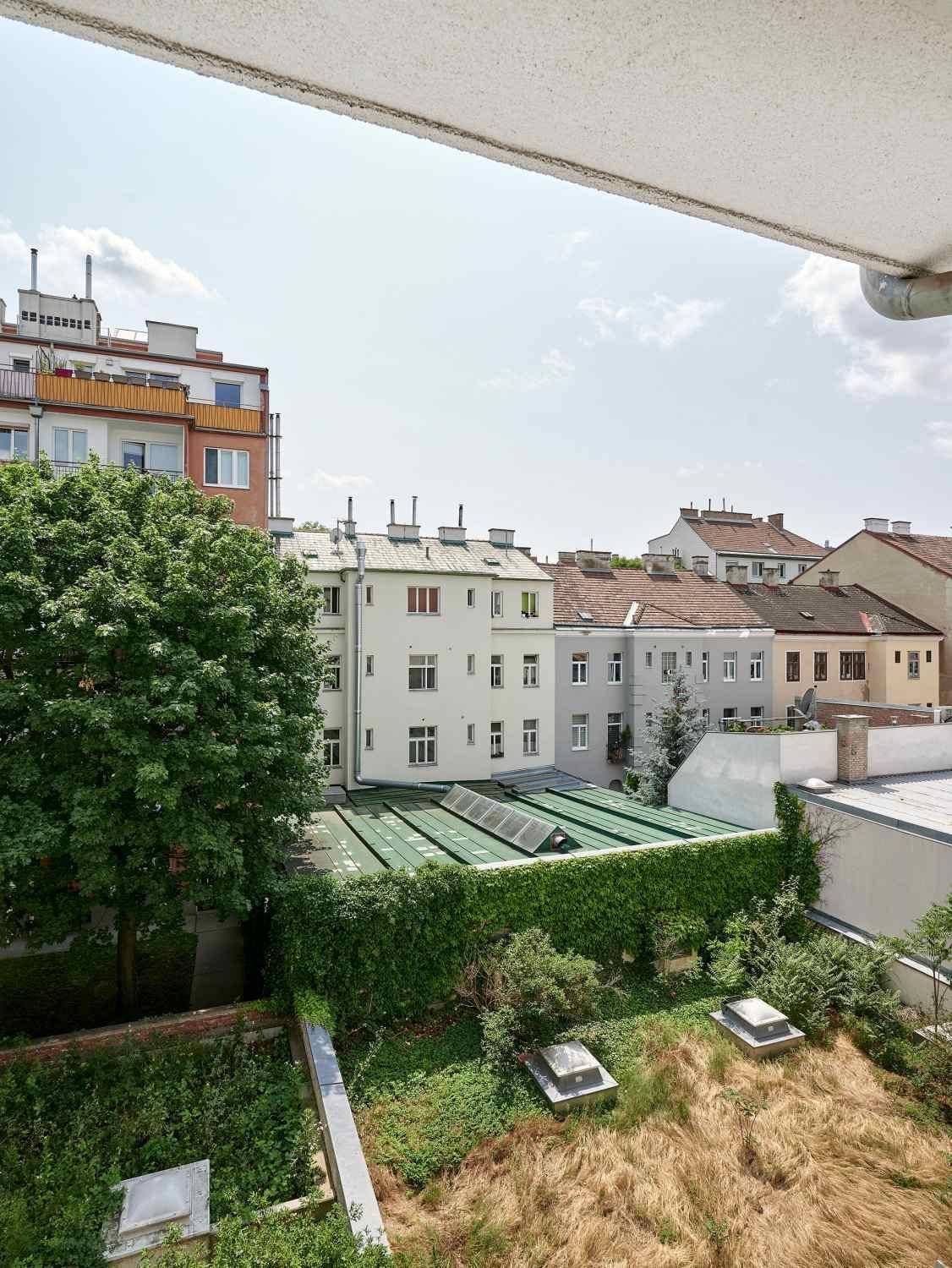 Blick von einem Balkon auf einen begrünten Innenhof und die umliegenden Stadtgebäude.