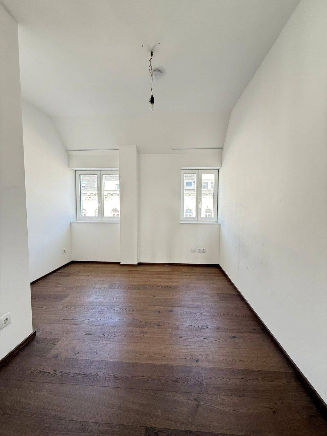 Helles Schlafzimmer mit Holzboden und zwei Fenstern, bereit zur individuellen Gestaltung.