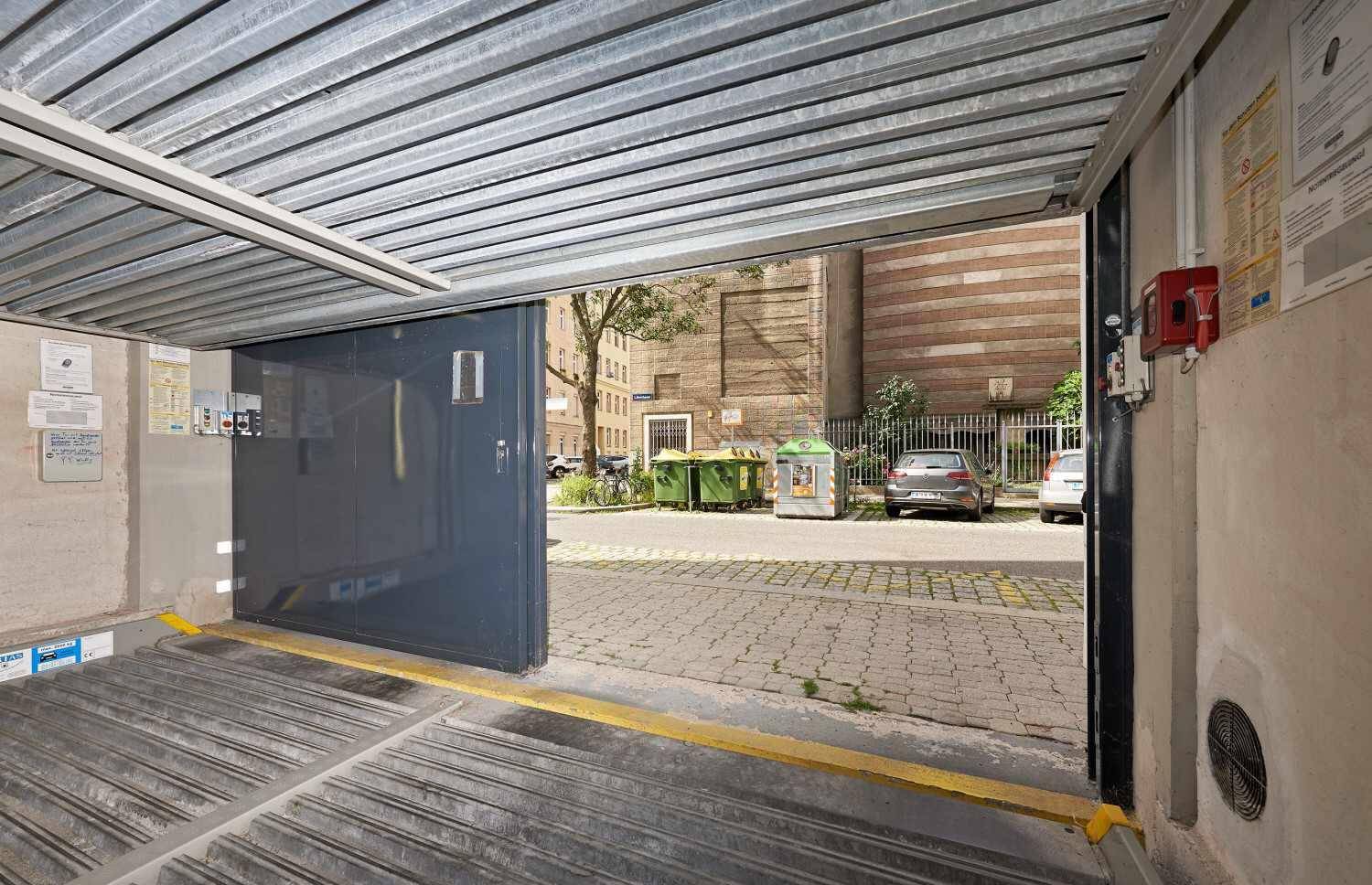 Blick aus der Tiefgarage auf die Straße mit Müllcontainern und parkenden Autos.
