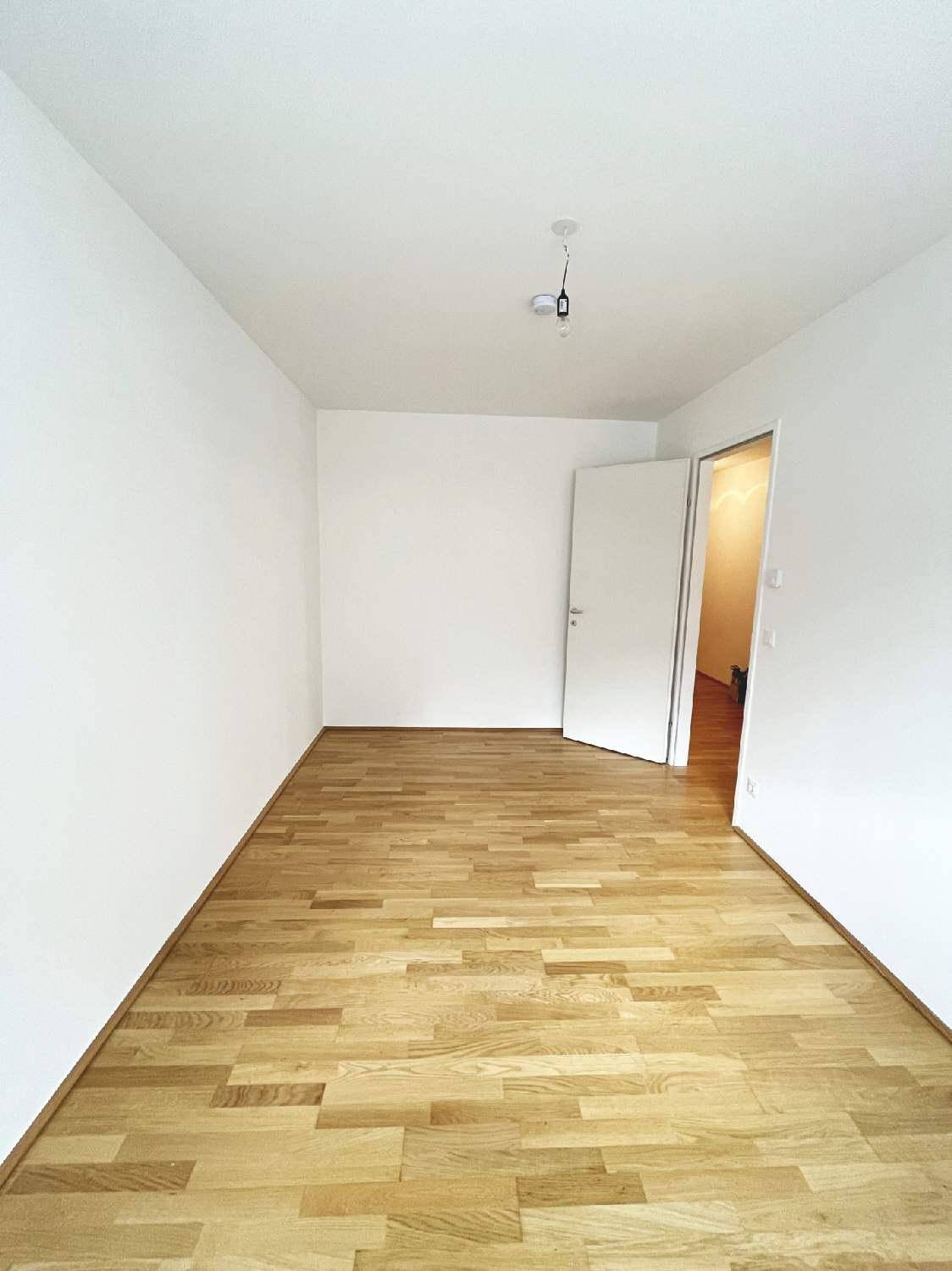 Leeres Schlafzimmer mit hellem Parkettboden und weiß gestrichenen Wänden.