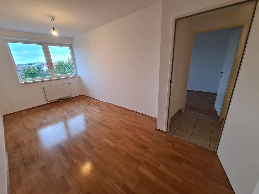 Helles Schlafzimmer mit glänzendem Holzboden und einem großen Fenster, das viel Licht hereinlässt.