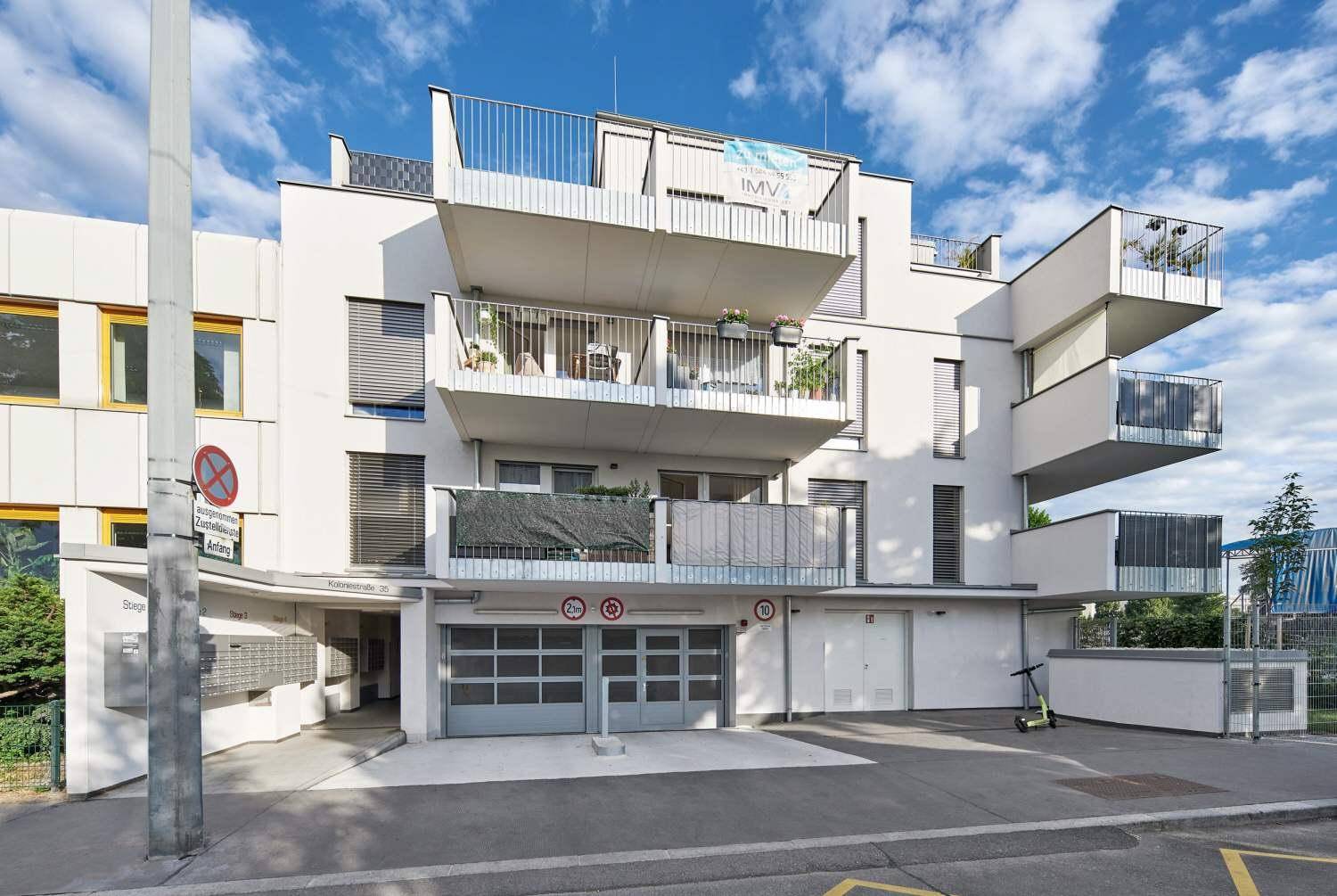 Ansicht des modernen Wohngebäudes mit Balkonen und Tiefgaragenzufahrt.