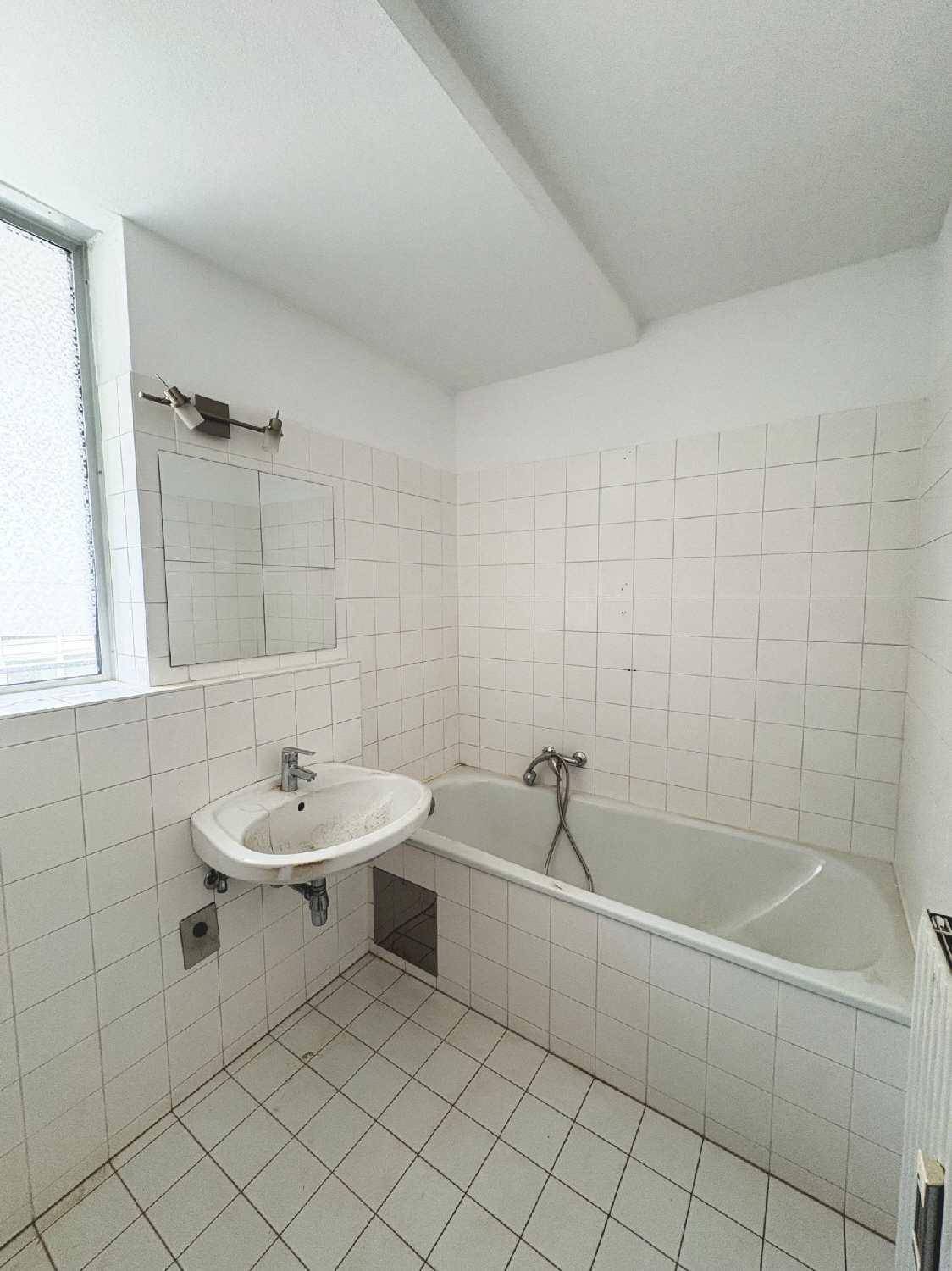 Helles Badezimmer mit weißen Fliesen, Badewanne, Waschbecken und einem Fenster für Tageslicht.