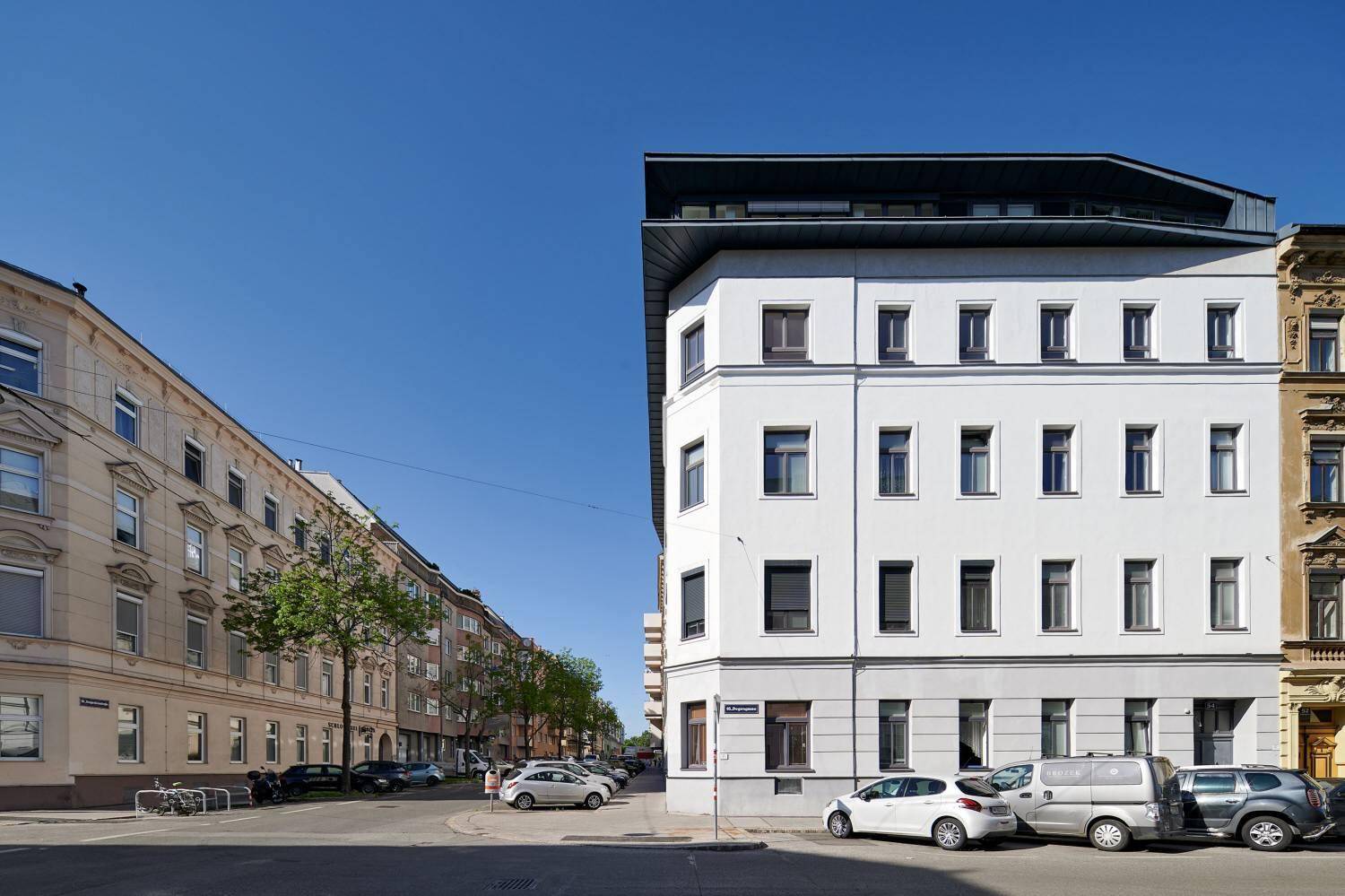 Eckansicht des modernen Gebäudes an einer belebten Straße mit weiteren Wohngebäuden im Hintergrund.