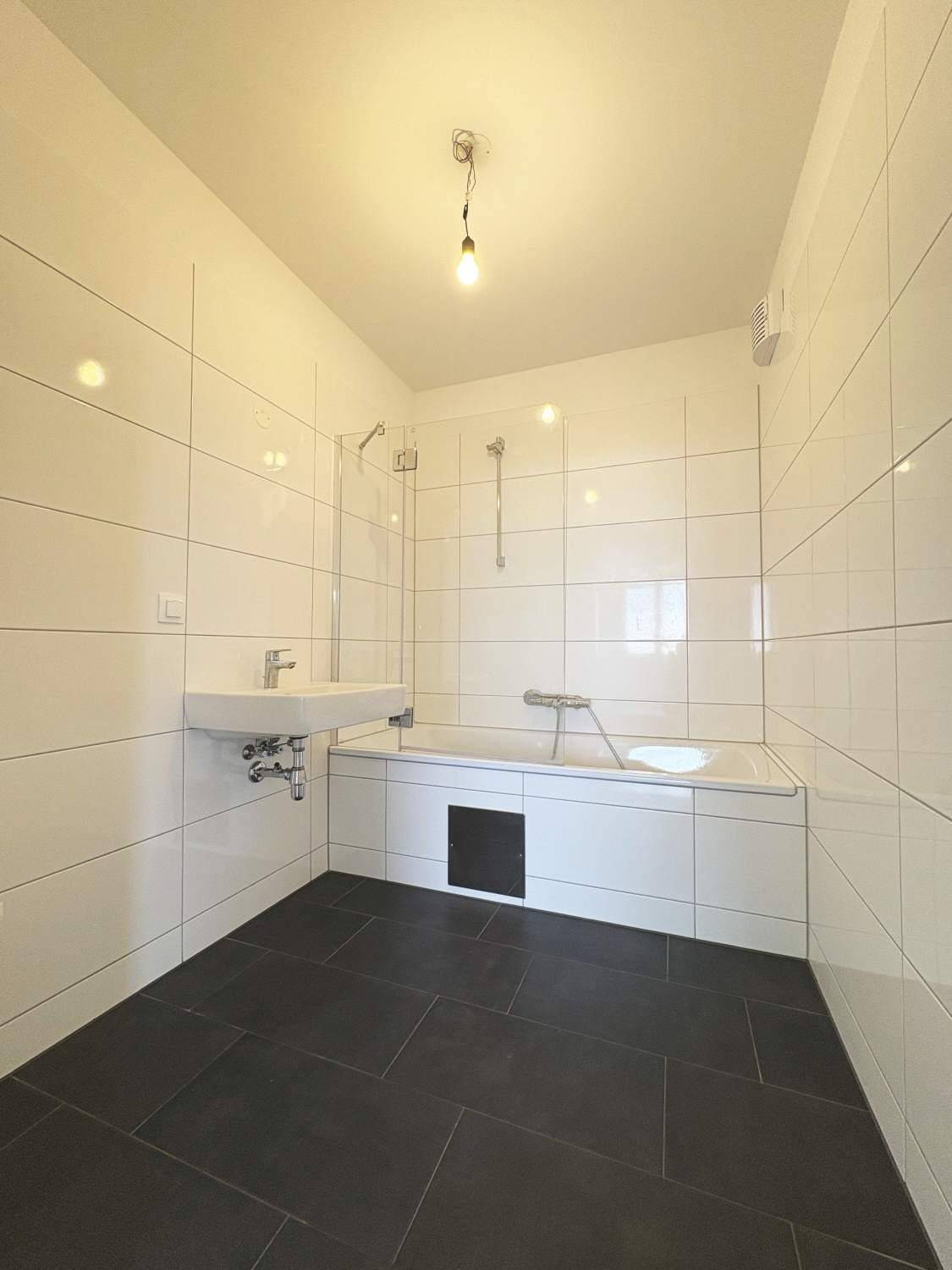 Modernes Badezimmer mit weißen Wandfliesen, dunklem Boden, Badewanne und schwebendem Waschbecken.