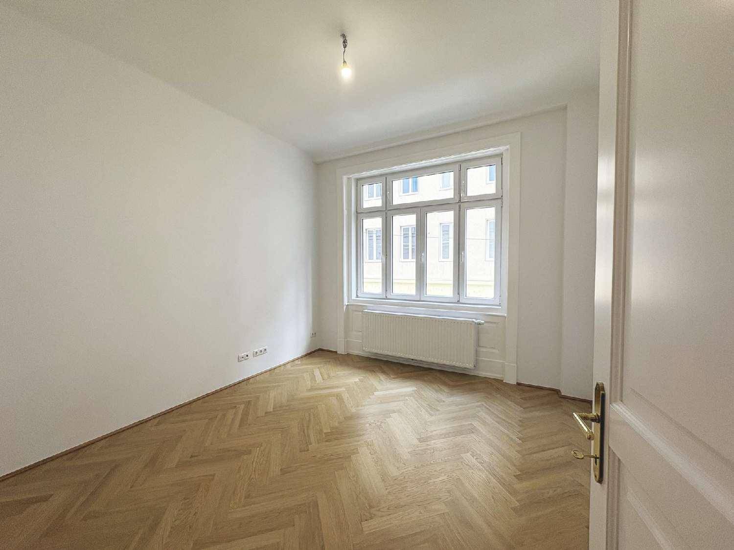 Helles Zimmer mit Fischgrätparkett und großem Fenster, bietet viel Tageslicht und eine angenehme Atmosphäre.
