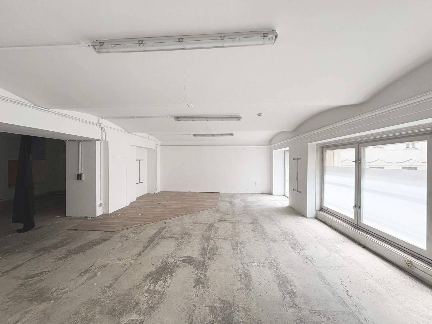 Heller, weitläufiger Gewerberaum mit großen Fenstern, weißen Wänden und einer Mischung aus Beton- und Holzfußboden.