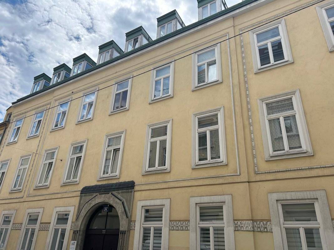Klassisches Mehrfamilienhaus mit gelber Fassade und vielen Fenstern unter bewölktem Himmel.