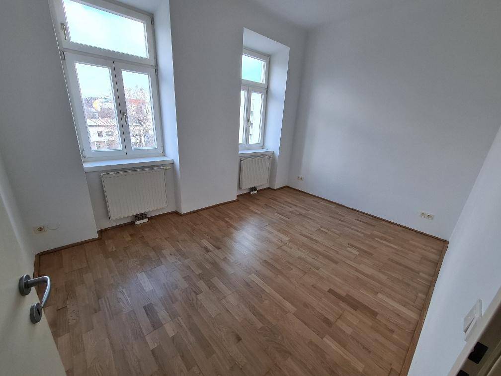 Leeres Zimmer mit Parkettboden und zwei Fenstern, ideal als Schlaf- oder Arbeitszimmer.