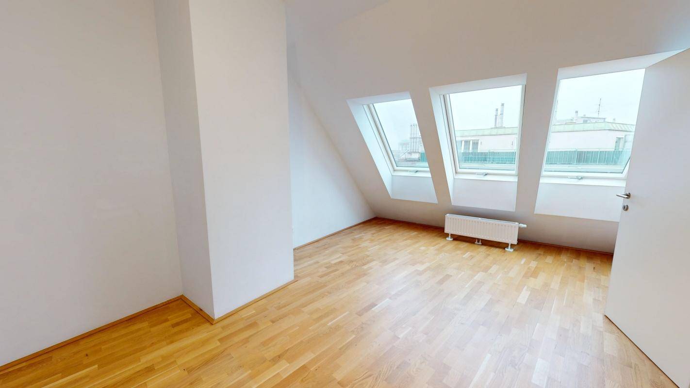 Lichtdurchfluteter Dachgeschossraum mit Holzboden und schrägen Wänden, bereit zur Einrichtung.
