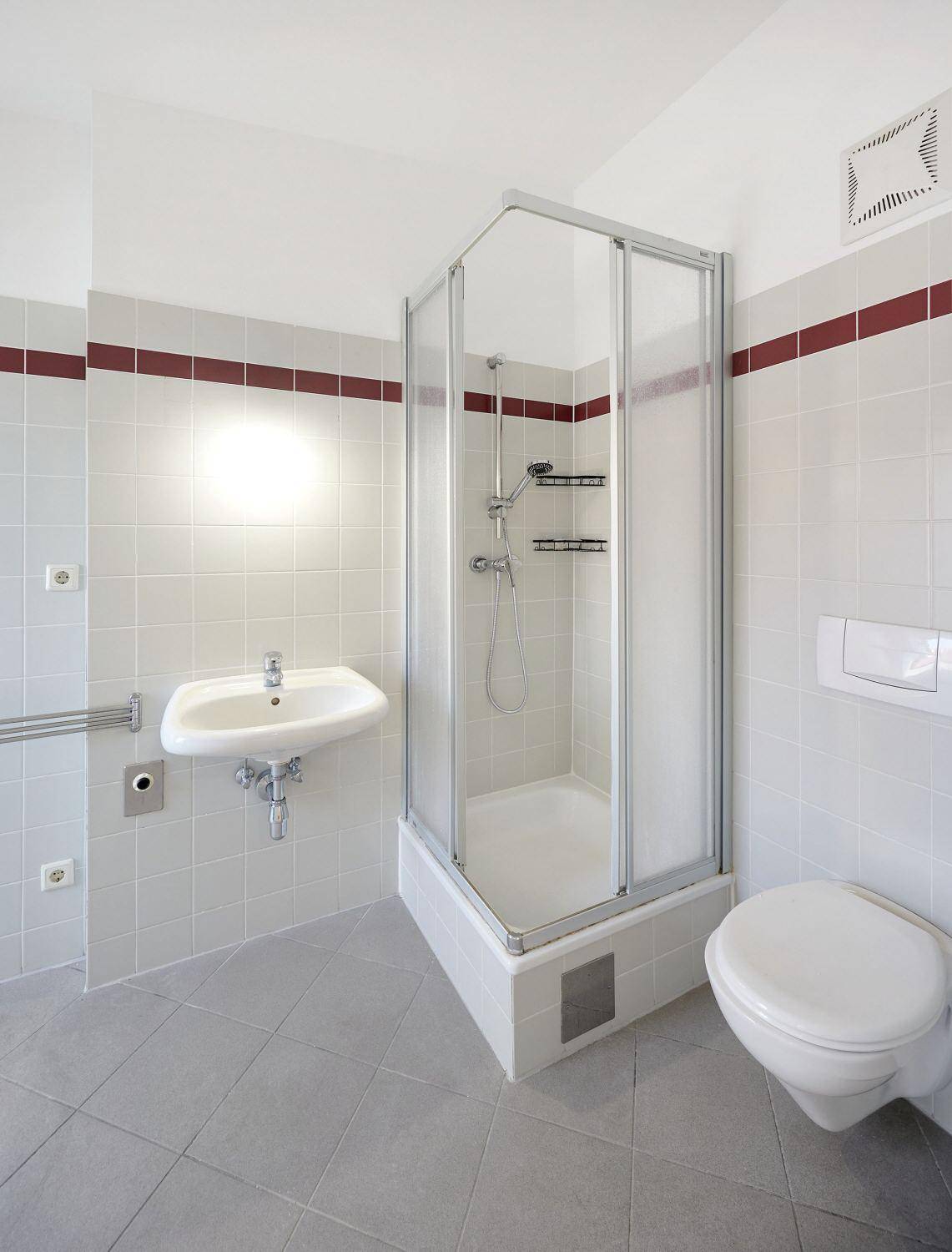 Modernes Badezimmer mit grauen Fliesen, Duschkabine, wandhängendem Waschbecken und WC.