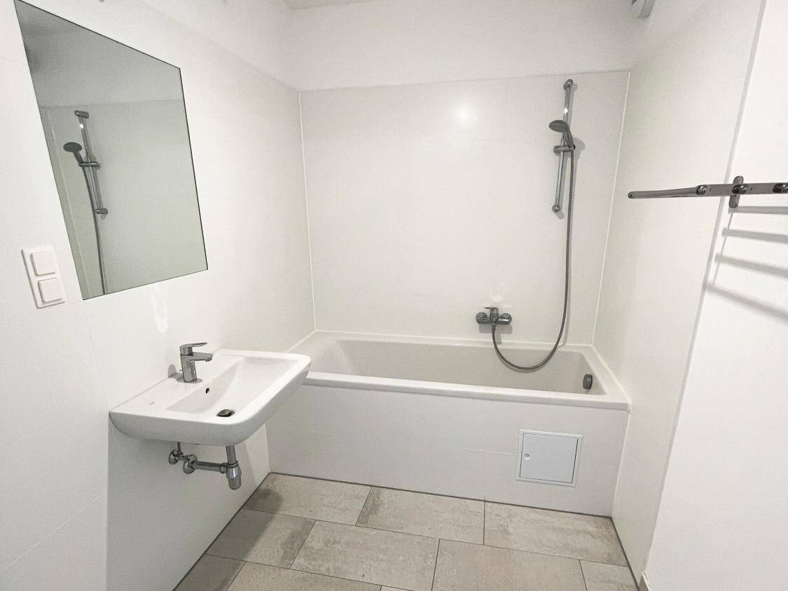 Modernes Badezimmer mit Badewanne inklusive Duschfunktion, Waschbecken und hellgrauen Fliesen, sehr gepflegt.