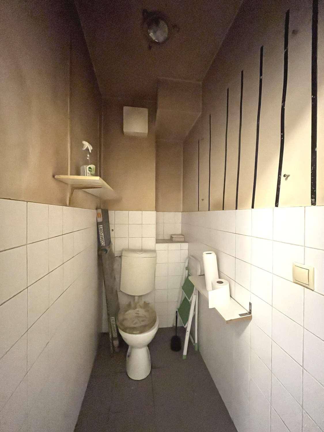Kleines WC mit weißen Fliesen und einfacher Toilette, in renovierungsbedürftigem Zustand.