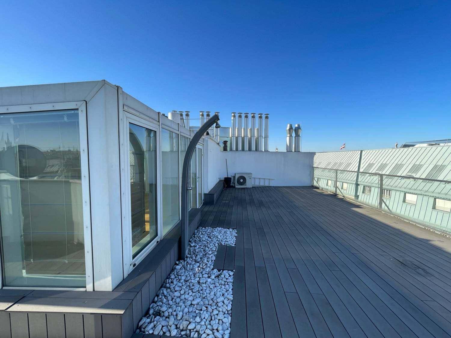 Große Dachterrasse mit Holzbelag, Außendusche und Blick auf die Stadt unter blauem Himmel.