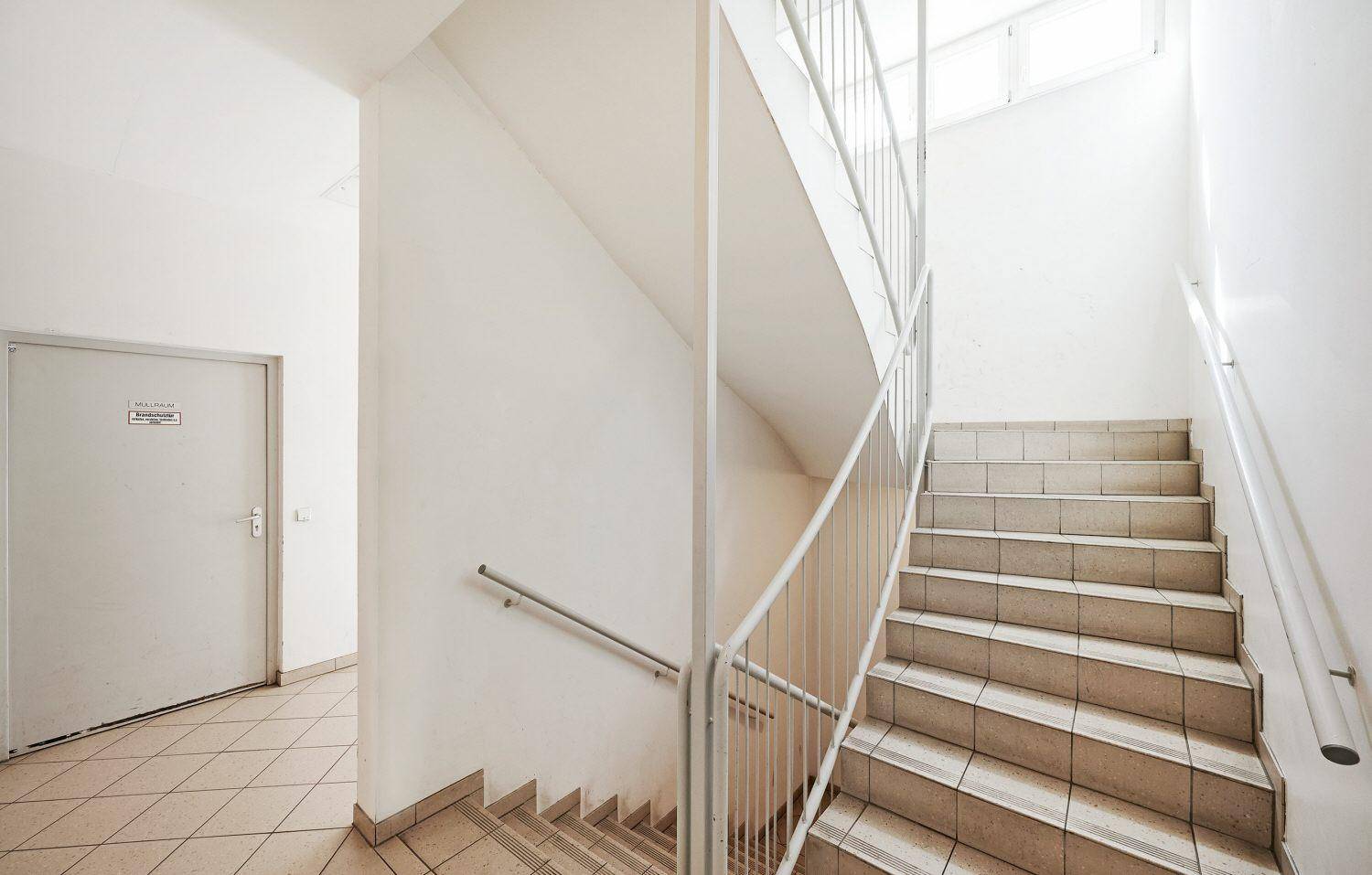 Treppenhaus mit gefliesten Stufen und Metallgeländer, das viel natürliches Licht von oben erhält.