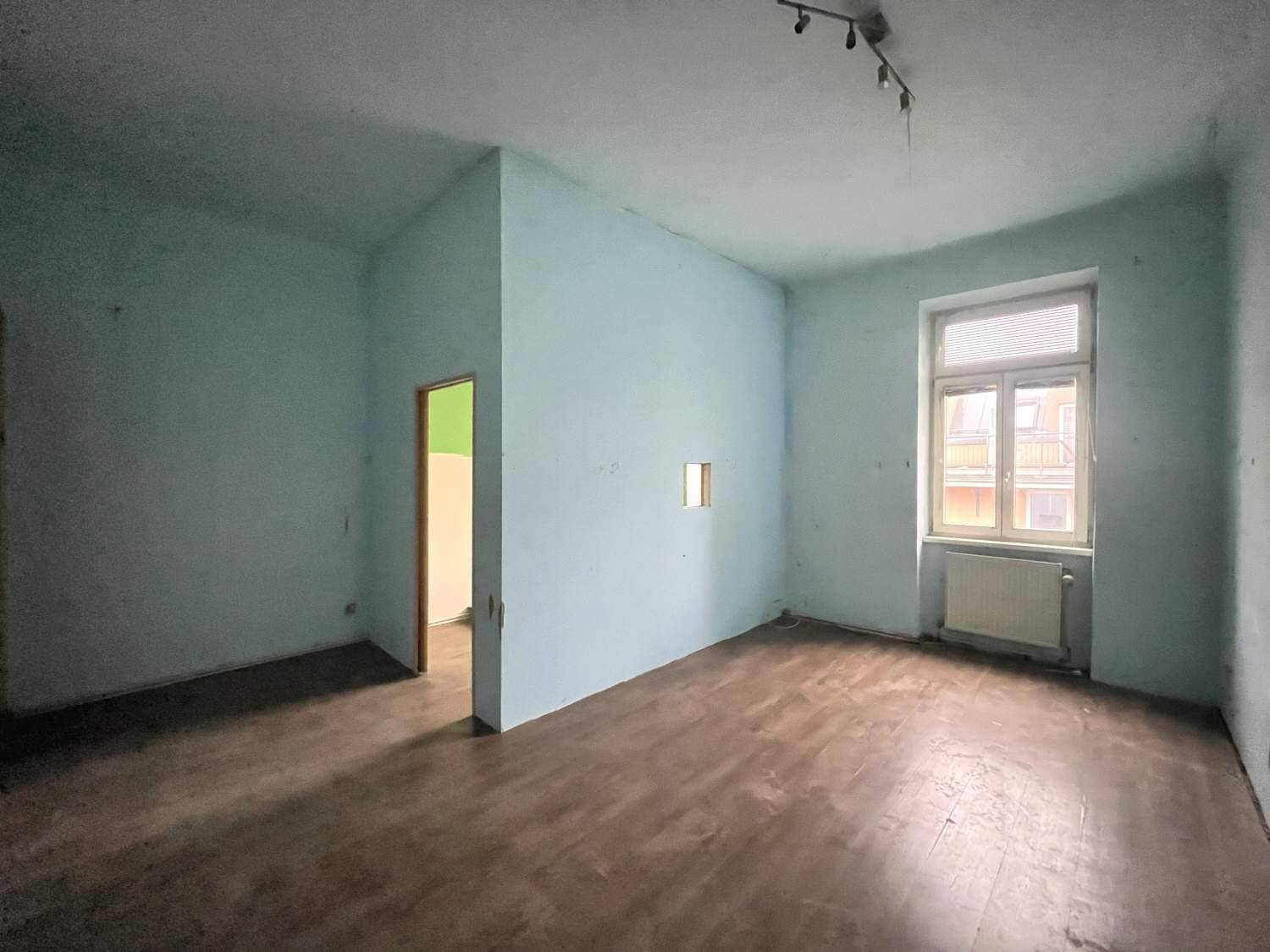 Leeres Zimmer mit hellblauen Wänden, Holzboden und einem Fenster.