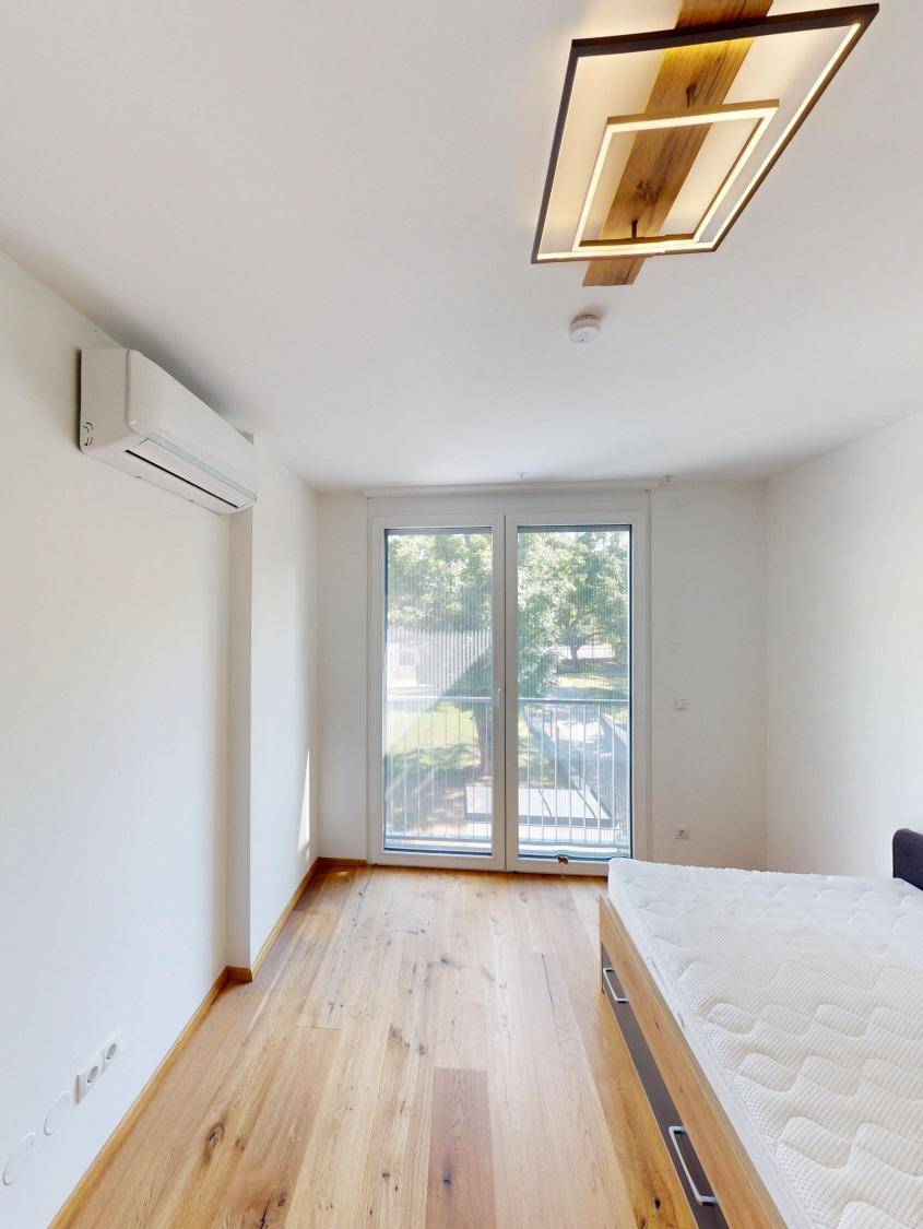 Schlafzimmer mit Holzboden, großen Fenstern und direktem Zugang zum Balkon.