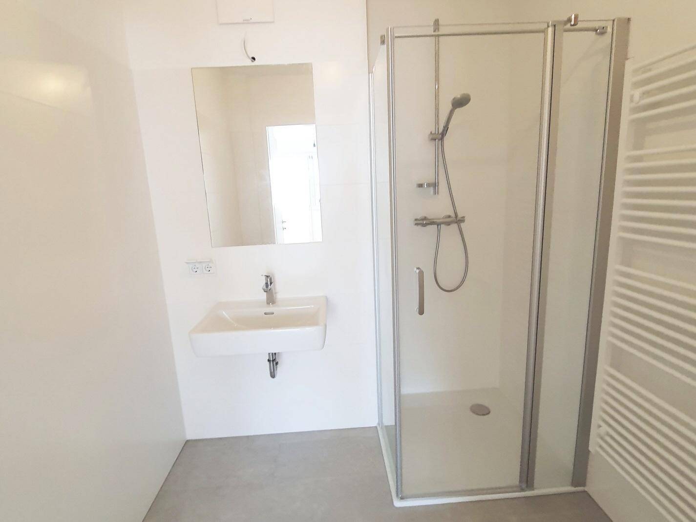 Modernes Badezimmer mit Duschkabine, wandhängendem Waschbecken und beheiztem Handtuchhalter.