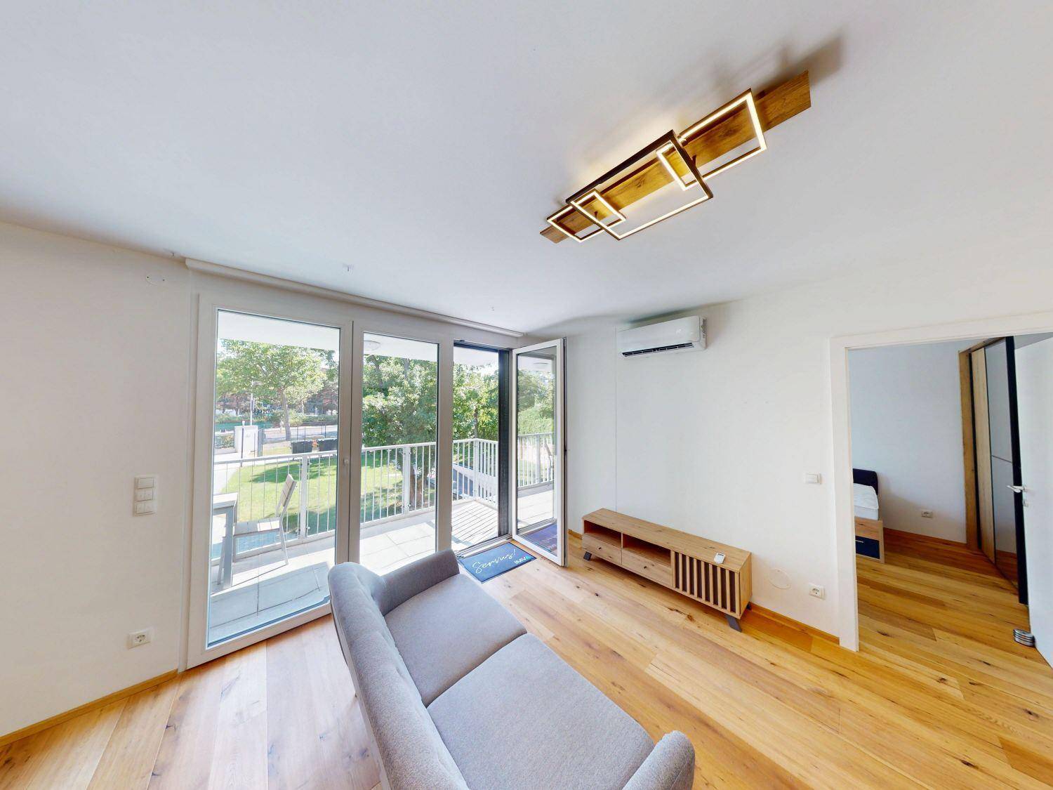 Helles Wohnzimmer mit Holzboden, minimalistischer Einrichtung und direktem Zugang zum Balkon.