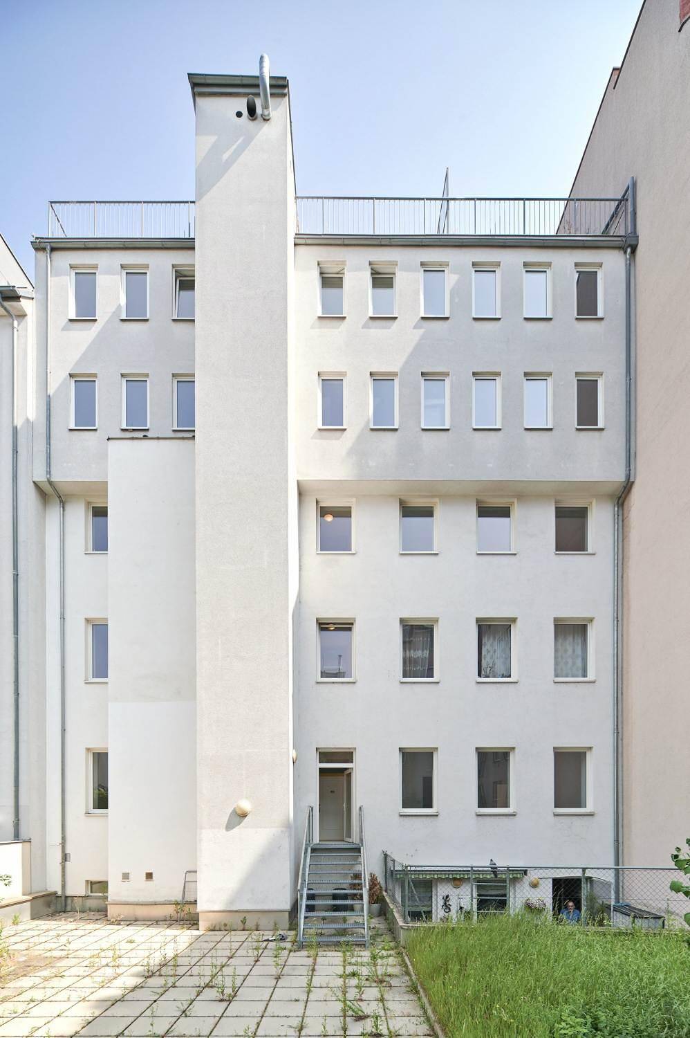 Rückseite eines Wohngebäudes mit vertikalem Schornstein und Zugang zum Gartenbereich.