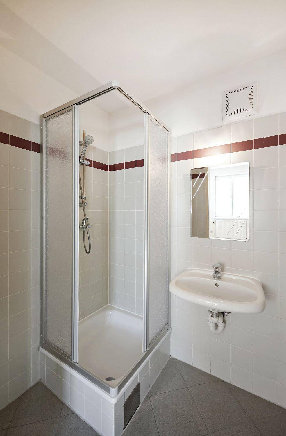 Badezimmer mit Duschkabine, Waschbecken und hellen Fliesen an Wänden und Boden.