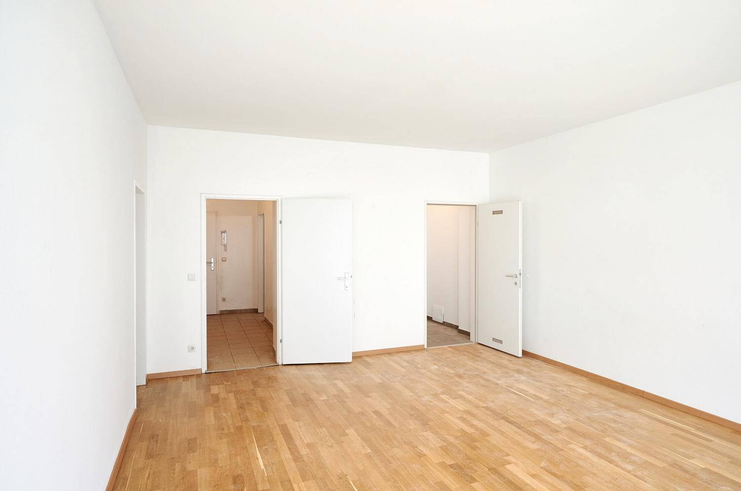 Geräumiges, leeres Zimmer mit Parkettboden und zwei offenen Türen, die zu weiteren Räumen führen.