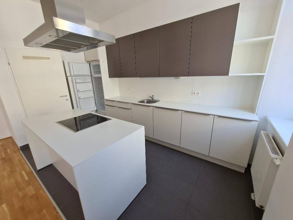 Moderne Einbauküche mit Kochinsel, Dunstabzugshaube und integriertem Kühlschrank in Weiß und Grau.