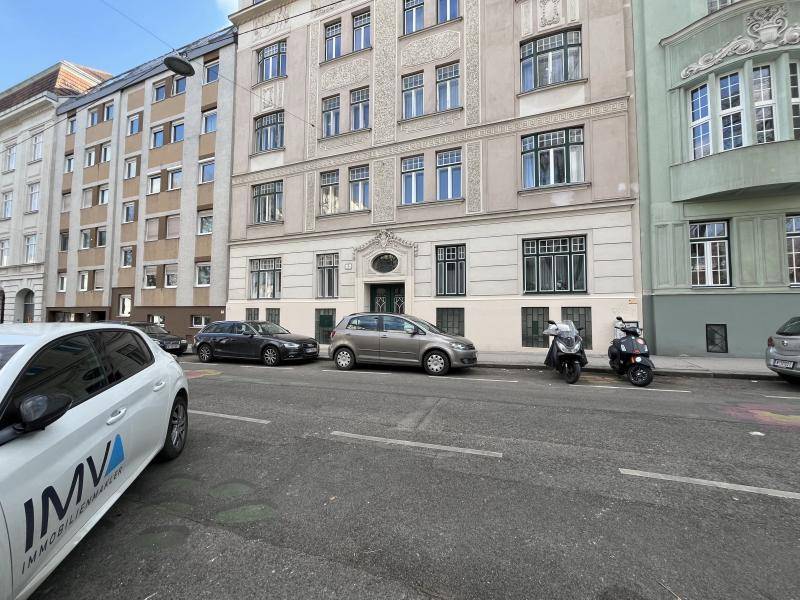 Straßenansicht eines Altbaus mit dekorativer Fassade und parkenden Autos vor dem Gebäude.