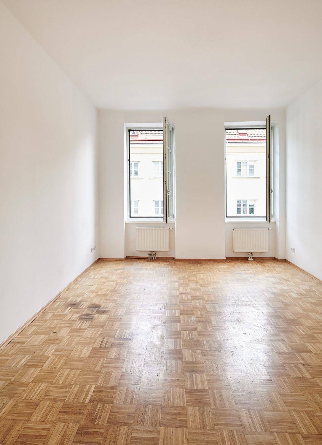 Geräumiges, helles Zimmer mit klassischem Parkettboden und Blick auf die umliegenden Gebäude.
