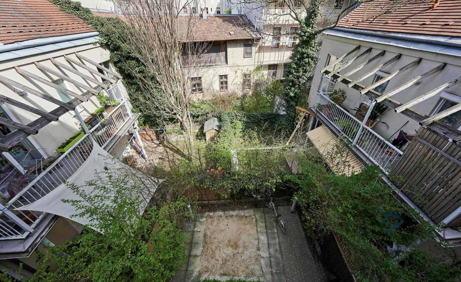 Blick von oben auf einen begrünten Innenhof mit Bäumen und einem Sandbereich.