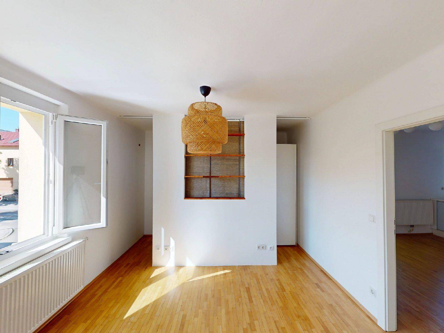 Helles Zimmer mit Parkettboden, großem Fenster und moderner Deckenleuchte.