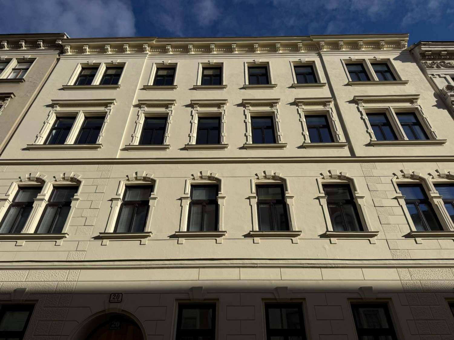 Historische Fassade eines Mehrfamilienhauses mit vielen Fenstern und architektonischen Details.