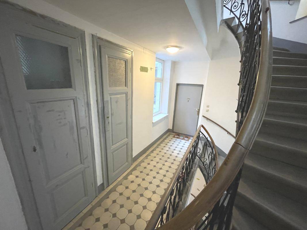 Treppenhaus mit geschwungener Treppe, alten Holztüren und gemustertem Fliesenboden.